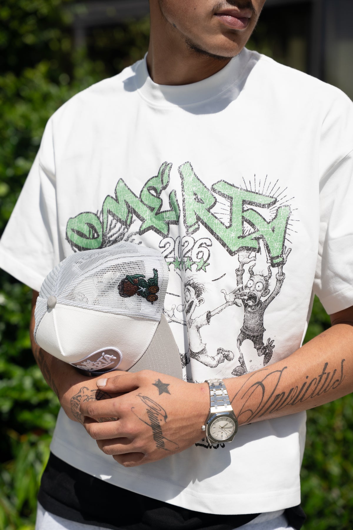 Close detail of the Omertà box-fit tee print and the signature trucker cap
